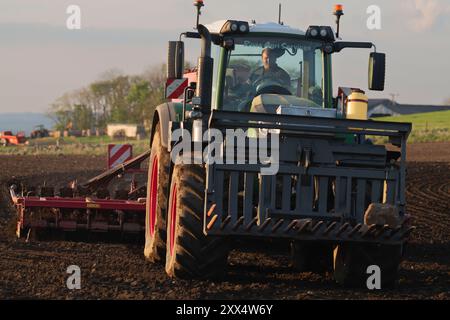 Vorderansicht eines Green Fendt-Traktors, der bei Abendsonne Gerste mit einer Scheibenbohrmaschine auf einem Pflugfeld aussät Stockfoto