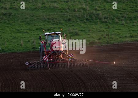 Eine Rückansicht eines Fendt-Traktors mit einer Horsch-Scheibenbohrmaschine, die im späten Frühlingsabend ein Feld mit Gerste säte Stockfoto