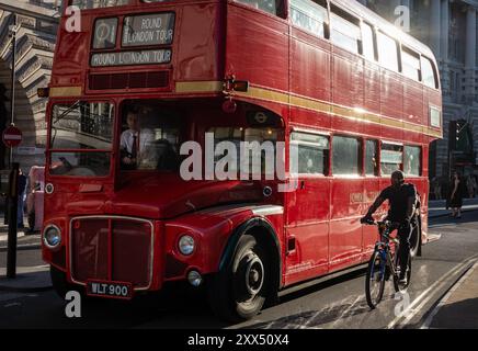 Ein traditioneller roter Routemaster London Bus, der für Touren durch London genutzt wird, fährt an einem Radfahrer vorbei. London, England, Großbritannien Stockfoto