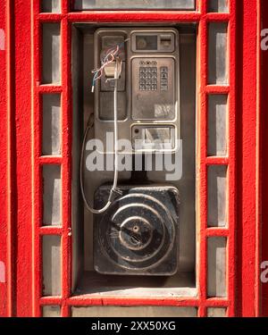 Ein beschädigtes öffentliches Münztelefon, das außerhalb eines traditionellen roten Telefonkiosks in London, Großbritannien, platziert wurde. Stockfoto