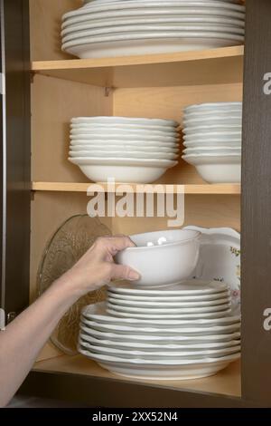 Vertikale Aufnahme der Hand einer Frau, die Geschirr in einem Küchenschrank ablegt. Stockfoto