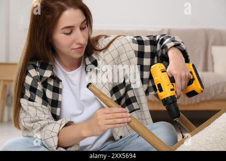 Frau mit elektrischem Schraubenzieher, der den Sessel zu Hause zusammenbaut Stockfoto