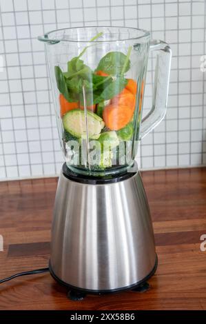 Mit Vitaminen verpackte Superfoods in einem Mixer zum Mischen bereit. Gesunde grüne Lebensmittel Spinat, Karotten, Rosenkohl und Brokkoli. Stockfoto