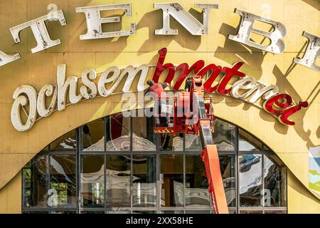 Aufbau Oktoberfest, Fachkräfte montieren die Neonschrift Ochsenbraterei am Festzelt, die Theresienwiese ist eine riesige Baustelle, München, August 2024 Deutschland, München, 22. August 2024, Aufbau Oktoberfest, Großbaustelle Theresienwiese, Fachkräfte montieren die Neonbuchstaben Ochsenbraterei, Spatenbräu, überall wird fleißig gehämmert und gezimmert, damit in vier Wochen zum Beginn der Wiesn 2024 alles perfekt ist, Sommer, Bayern, bayerisch, *** Oktoberfest Construction, Facharbeiter montieren das Neonschild Ochsenbraterei auf dem Festzelt, die Theresienwiese ist eine riesige Baustelle, Mun Stockfoto