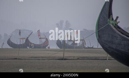 Traditionelle Mondboote (Shander Nouka), die bei Flut am Strand gelangten, nachdem sie die Brandung vor Cox's Bazar in Bangladesch überquert hatten. Diese mondförmigen Fischerboote tragen in der Regel eine Besatzung von 3 bis 5 Personen und sind für ihre wunderschöne Handwerkskunst bekannt. Die Form macht sie perfekt für die Überquerung der Brandung, um zu den Angelplätzen zu gelangen. Die hohe Partikelverschmutzung durch die Ziegelproduktion entlang des Deltas lässt den Himmel mit Smog trüben. Stockfoto