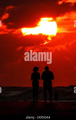 Isle Of Palms, Usa. August 2024. Ein Paar beobachtet, wie die Sonne über Sturmwolken am Atlantikhorizont bei Sonnenaufgang am Strand von Wild Dunes, 22. August 2024 in Isle of Palms, South Carolina, drückt. Quelle: Richard Ellis/Richard Ellis/Alamy Live News Stockfoto