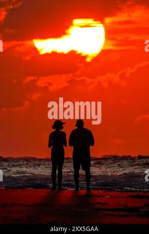Isle Of Palms, Usa. August 2024. Ein Paar beobachtet, wie die Sonne über Sturmwolken am Atlantikhorizont bei Sonnenaufgang am Strand von Wild Dunes, 22. August 2024 in Isle of Palms, South Carolina, drückt. Quelle: Richard Ellis/Richard Ellis/Alamy Live News Stockfoto