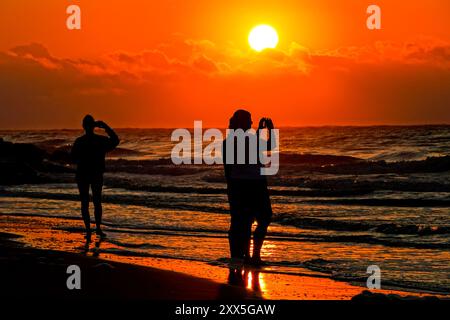 Isle Of Palms, Usa. August 2024. Strandbesucher machen Fotos von der Sonne, die bei Sonnenaufgang über eine Sturmwolke blickt, am Strand von Wild Dunes, 21. August 2024 in Isle of Palms, South Carolina. Quelle: Richard Ellis/Richard Ellis/Alamy Live News Stockfoto
