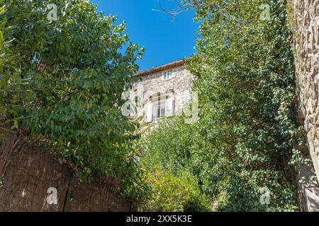 Ein einzelnes Fenster in einem alten Steingebäude, umgeben von grünem Laub. Aufgenommen in Vezenorbes, Provence, Frankreich an einem sonnigen Augusttag Stockfoto