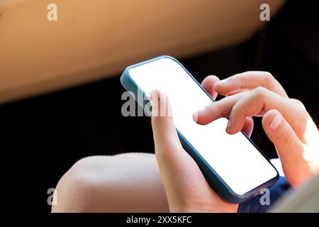 Die Hände des kleinen Jungen halten ein Telefon mit einem weißen Bildschirm während des Tages in der Sonne, halten das Telefon Stockfoto