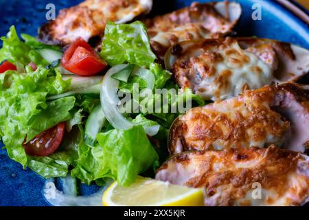 Fisch Und Meeresfrüchte. Muschelmuscheln. Gebackene Muscheln mit Käse, Koriander und Zitrone in Schalen auf gusseiserner schwarzer Platte. Teller mit Muscheln, kaltem Weißwein, Zitrone Stockfoto