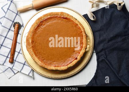 Frisch gebackener hausgemachter Kürbiskuchen auf einem weißen Holztisch mit Schürze, Nudelnadel und Crimper. Stockfoto