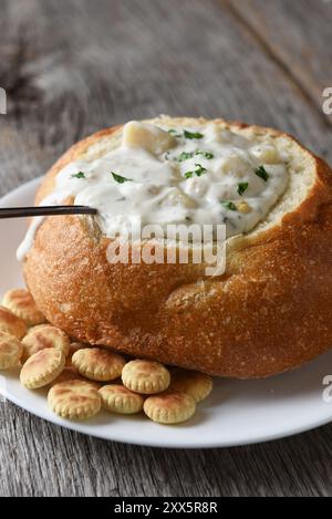 Vertikale Nahaufnahme von einem Brot Schüssel von New England Clam Chowder auf einem rustikalen Holztisch mit einem Löffel und Oyster Cracker. Stockfoto