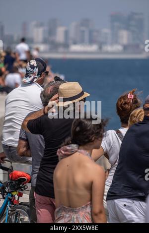 Barcelona, Spanien. August 2024. Ein Zuschauer hält seinen windgepeitschten Hut unter einer großen Gruppe von Leuten, die die erste Vorrunde des America's Cup Segelrennen vom Küstenmeer aus beobachten. Die Louis Vuitton Preliminary Regatta 2024 America's Cup hat heute Morgen die ersten Vorläufe gestartet. Besucher, Touristen und Einwohner konnten das erste Rennen des Wettbewerbs kostenlos von den Aussichtspunkten an der Küste und auf großen Bildschirmen in den Fan Zones genießen. Quelle: SOPA Images Limited/Alamy Live News Stockfoto