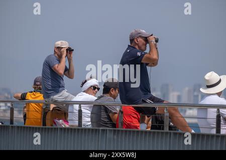 Barcelona, Spanien. August 2024. Zwei Personen sehen sich den America's Cup-Wettbewerb mit einem Fernglas vom Steg aus an. Die Louis Vuitton Preliminary Regatta 2024 America's Cup hat heute Morgen die ersten Vorläufe gestartet. Besucher, Touristen und Einwohner konnten das erste Rennen des Wettbewerbs kostenlos von den Aussichtspunkten an der Küste und auf großen Bildschirmen in den Fan Zones genießen. Quelle: SOPA Images Limited/Alamy Live News Stockfoto