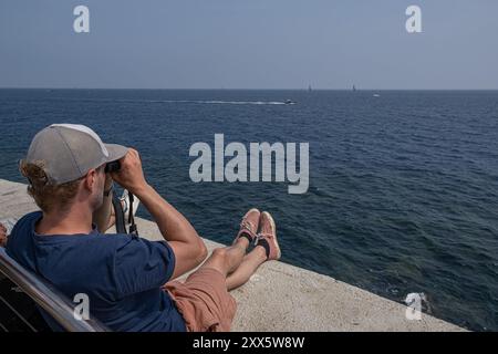 Barcelona, Spanien. August 2024. Ein junger Mann sieht die Regatta mit einem Fernglas vom Steg aus. Die Louis Vuitton Preliminary Regatta 2024 America's Cup hat heute Morgen die ersten Vorläufe gestartet. Besucher, Touristen und Einwohner konnten das erste Rennen des Wettbewerbs kostenlos von den Aussichtspunkten an der Küste und auf großen Bildschirmen in den Fan Zones genießen. Quelle: SOPA Images Limited/Alamy Live News Stockfoto