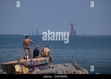 Barcelona, Spanien. August 2024. Am Strand beobachten drei Menschen die Segelboote, die während des Vorwettbewerbs zum American Cup vorbeifahren. Der Louis Vuitton Preliminary Regatta 2024 America's Cup hat heute Morgen die ersten Vorläufe gestartet. Besucher, Touristen und Einwohner konnten das erste Rennen des Wettbewerbs kostenlos von den Aussichtspunkten an der Küste und auf großen Bildschirmen in den Fan Zones genießen. Quelle: SOPA Images Limited/Alamy Live News Stockfoto