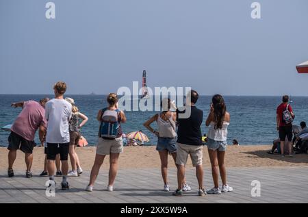 Barcelona, Spanien. August 2024. Eine Gruppe von Kinderwagen am Strand ist von der Nähe eines der America's Cup Segelboote überrascht. Die Louis Vuitton Preliminary Regatta 2024 America's Cup hat heute Morgen die ersten Vorläufe gestartet. Besucher, Touristen und Einwohner konnten das erste Rennen des Wettbewerbs kostenlos von den Aussichtspunkten an der Küste und auf großen Bildschirmen in den Fan Zones genießen. Quelle: SOPA Images Limited/Alamy Live News Stockfoto