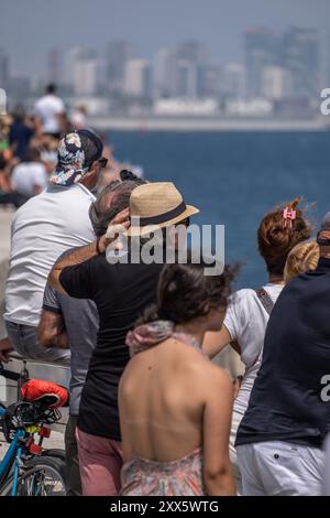 Barcelona, Spanien. August 2024. Ein Zuschauer hält seinen windgepeitschten Hut unter einer großen Gruppe von Leuten, die die erste Vorrunde des America's Cup Segelrennen vom Küstenmeer aus beobachten. Die Louis Vuitton Preliminary Regatta 2024 America's Cup hat heute Morgen die ersten Vorläufe gestartet. Besucher, Touristen und Einwohner konnten das erste Rennen des Wettbewerbs kostenlos von den Aussichtspunkten an der Küste und auf großen Bildschirmen in den Fan Zones genießen. (Foto: Paco Freire/SOPA Images/SIPA USA) Credit: SIPA USA/Alamy Live News Stockfoto