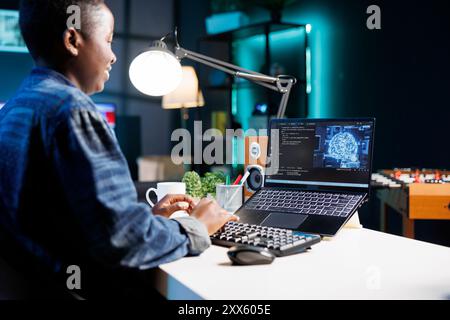 Weibliche Entwicklercodierung für KI und maschinelles Lernen auf digitalen Laptops. Schwarze Frau, die auf ihrem PC auf neuronales Netzwerk und Datenbank blickt, während sie auf der Tastatur schreibt. Stockfoto