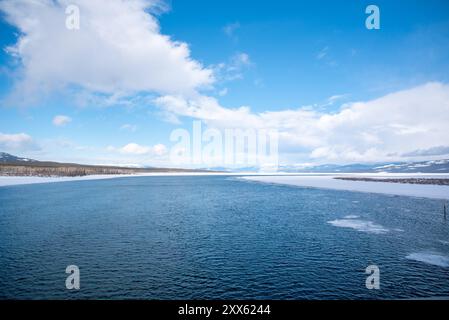 Ein blauer, heller Tag mit teilweise bewölkten Wolken und einem großen Fluss mit schneebedeckten Bergen und schneebedeckter Landschaft in Tagish, Yukon, Kanada Stockfoto