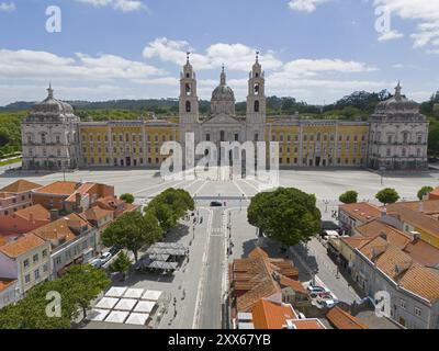 Historischer barocker Palast mit gelber Fassade und zwei Türmen, unter blauem Himmel und großem Platz, Blick aus der Luft, Palast, Palacio Nacional de Mafra, Li Stockfoto