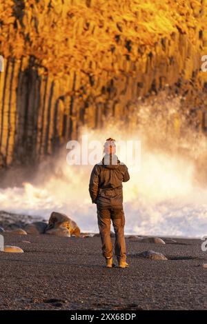 Ein Tourist am schwarzen Sandstrand von Reynisfjara bei Sonnenuntergang in Island Stockfoto