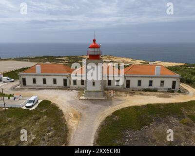 Leuchtturm und langes Gebäude entlang der Küste, mit Blick auf das Meer und den bewölkten Himmel, Luftsicht, Farol do Cabo Sardao, Sardao, Ponta do Cavaleiro, Ode Stockfoto