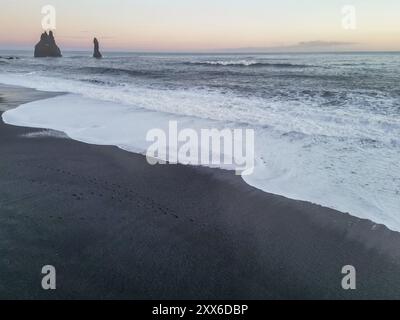 Drohnenblick auf den schwarzen Sandstrand von Reynisfjara bei Sonnenuntergang in Island Stockfoto