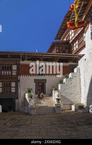 Zwei glückliche bhutanische Kinder in bunten Kleidern, die die Treppe hoch im Hinterhof von Trongsa Dzong, Bhutan, Asien Stockfoto