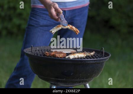 Ein Mann, der eine Wurst auf dem Grill hält Stockfoto