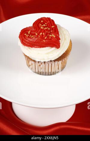 Fantasievoller Valentinstag-Cupcake mit roter Herzform auf einem weißen Tablett auf rotem Hintergrund. Mit Copyspace Stockfoto