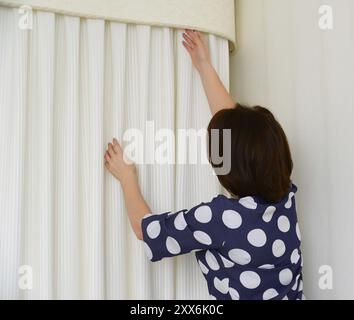 Frau, die weiße Vorhänge an das Fenster in der Wohnung hängt Stockfoto