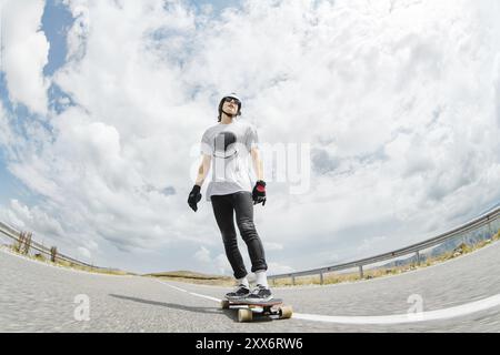 Der Typ mit Helm und Sonnenbrille fährt sehr schnell auf der Asphaltstraße in einem Standständer mit seinem Longboard Stockfoto