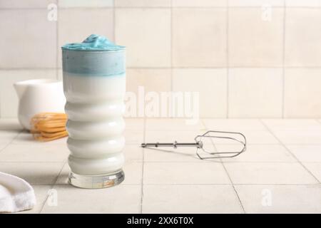 Glas blauer Dalgona Matcha Latte und Mixer-Schneebesen auf Fliesentisch Stockfoto