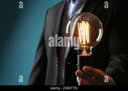 Geschäftsmann mit glühender Glühbirne auf blauem Hintergrund, Nahaufnahme Stockfoto