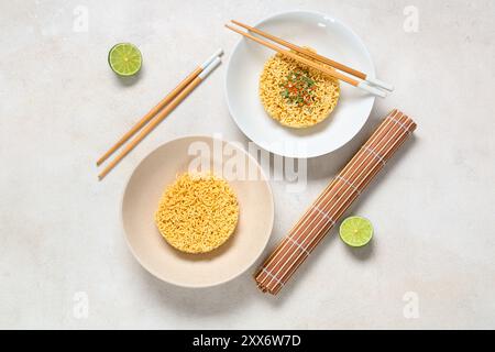 Schüsseln mit rohen Instant-Nudeln, Gewürz, Limette und Holzstäbchen auf weißem Hintergrund Stockfoto