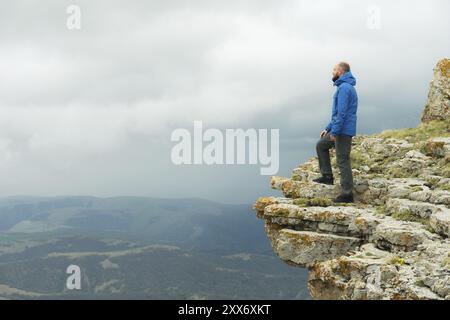 Bärtiger Hipster-Tourist, der am Felsenrand steht und auf einem epischen Plateau in die Ferne blickt. Das Konzept des Tourismus Stockfoto