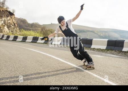 Ein junger Fahrer auf einem Longboard mit Helm und Handschuhen macht einen Speed Slide mit Geschwindigkeit, während er wieder auf einer Bergstraße in den Bergen fährt Stockfoto