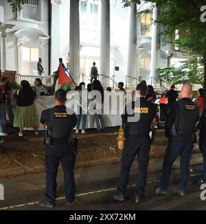 Raleigh, NC, USA, 22. August 2024; die Polizei beobachtet rund vierzig Demonstranten, die Schilder halten, Fahnen schwenken und Anti-Kriegs- und Anti-Demokratische Parolen über den Israel-Hamas-Krieg im Gazastreifen singen. Der Protest fand vor dem Hauptquartier der North Carolina Democratic Party in Raleigh während der letzten Nacht des Democratic National Convention statt. Credit D Guest Smith / Alamy Live News Stockfoto