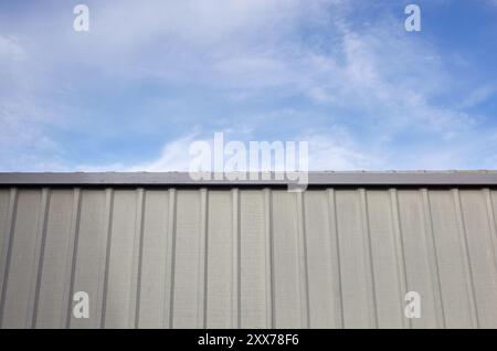 Gewellter Stahlzaun gegen blauen Himmel. Oberfläche mit gewellter Metallstruktur oder galvanisiertem Stahl Stockfoto