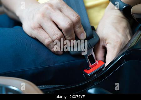 Knick Nach Oben. Nahaufnahme eines Mannes, der den Sicherheitsgurt im Auto anlegt, Mittelteil. Hände ein Gurtschloss im Fahrgastraum des Beifahrers anlegen und lösen. Stockfoto