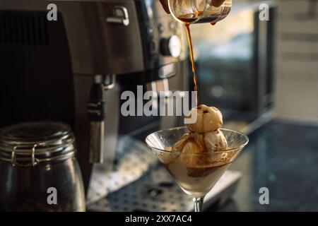 Cremiges Eis wird in einer Glasschale gegenüber einer Kaffeemaschine mit Kaffee übergossen. Stockfoto