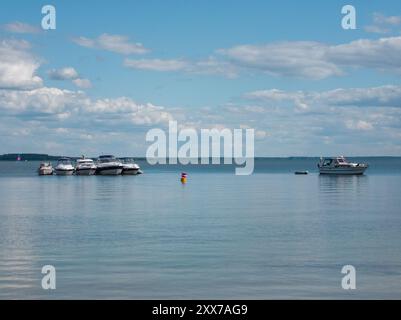 Mehrere Boote liegen an einem ruhigen See unter blauem Himmel mit weißen Wolken. Ein einzelnes Boot liegt weiter draußen im See vor Anker. Stockfoto