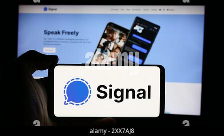 Person, die ein Mobiltelefon mit dem Logo des Open-Source-Instant Messaging-Dienstes Signal vor der Webseite hält. Schwerpunkt auf dem Display des Telefons. Stockfoto