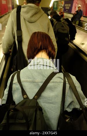 Eine Frau mit rotem Haarschnitt und einem dünnen Tattoo, das auf einer Rolltreppe an einem Bahnhof in Sydney am Nacken entlang läuft Stockfoto