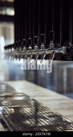 Reihe von Bierhähnen aus glänzendem Chrom mit schwarzen Griffen, über der Arbeitsplatte mit Metallabtropfschale positioniert. Stockfoto