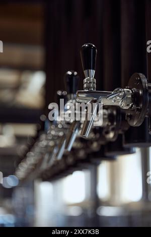Nahaufnahme einer Reihe glänzender Chrom-Bierhähne mit schwarzen Griffen, auf dunklem Hintergrund montiert. Moderne Bierbrauerei Stockfoto