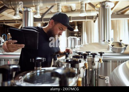 Konzentrierter und aufmerksamer Mann, Brauereitechniker, der Ventile und Manometer anpasst, verkörpert das Know-how, das in der modernen Bierherstellung erforderlich ist. Stockfoto