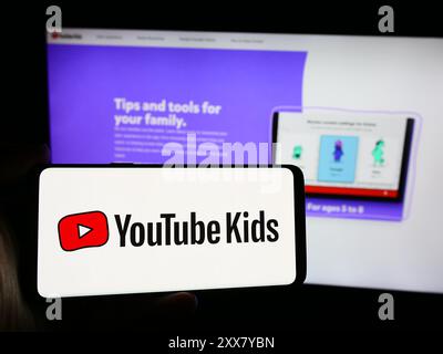 Person, die ein Smartphone mit dem Logo des US-amerikanischen Unternehmens YouTube Kids vor der Website hält. Schwerpunkt auf dem Display des Telefons. Stockfoto
